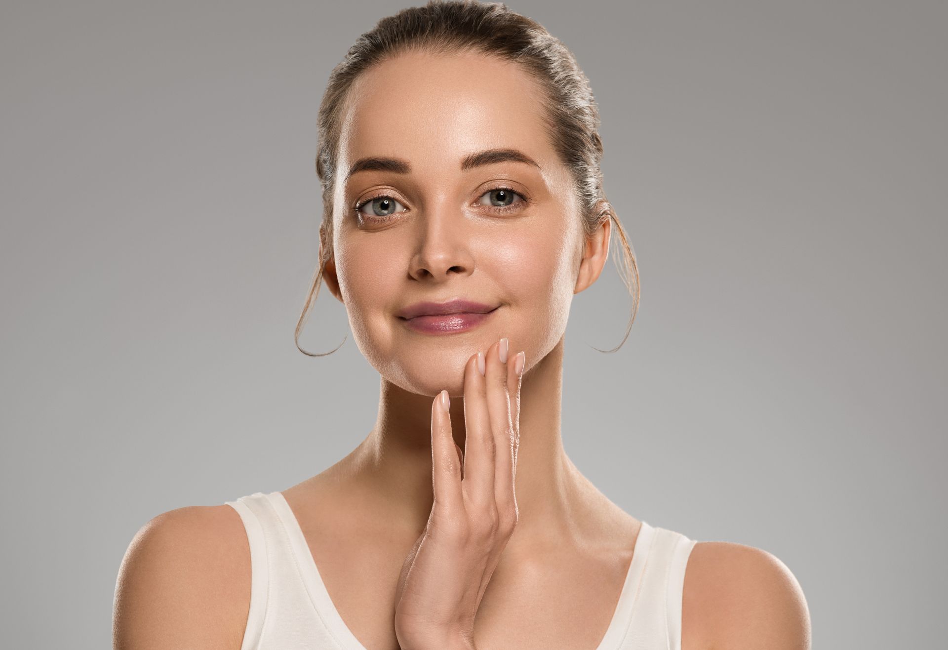 A woman is touching her face with her hands and smiling.