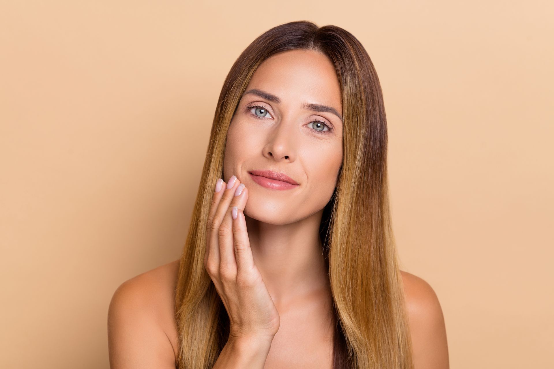 Woman gently touching her cheek on a beige background.