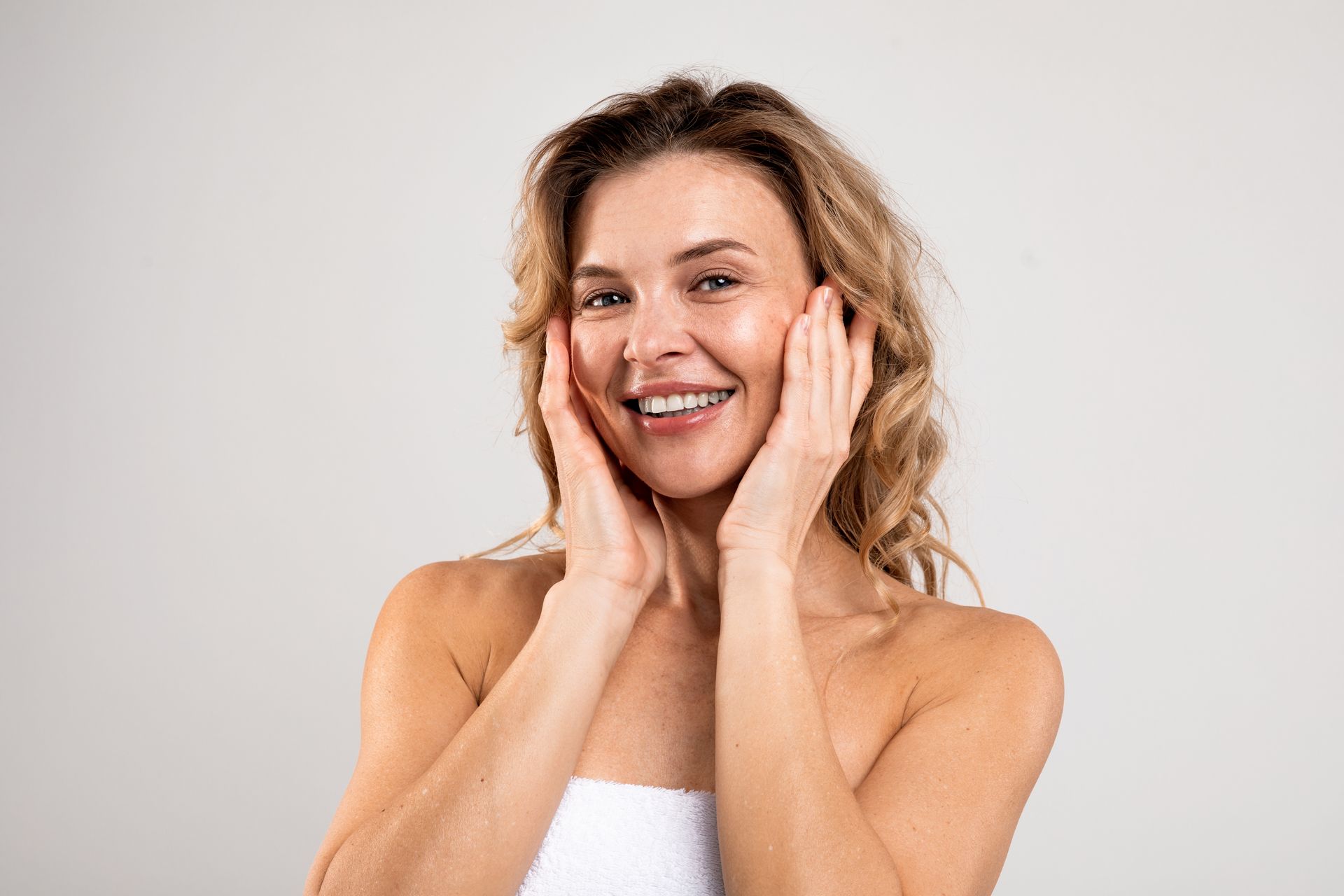 A woman is smiling and touching her face with her hands.