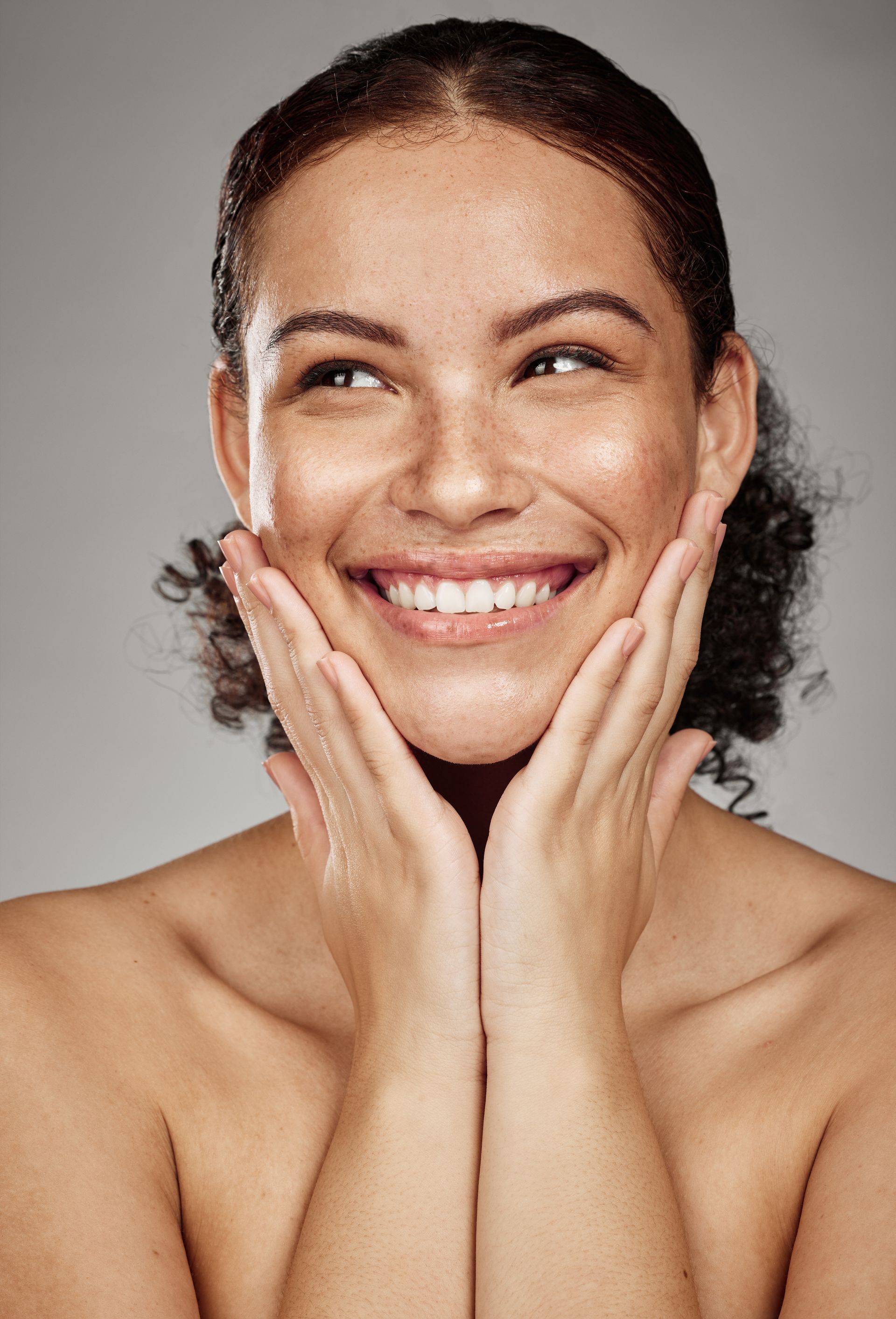 A woman is smiling and touching her face with her hands.