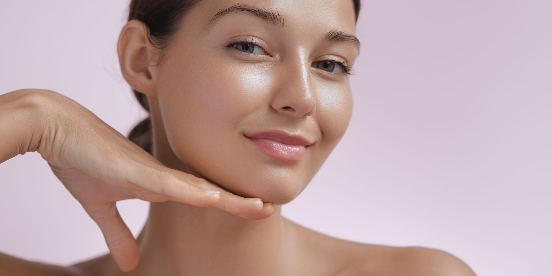 A woman is touching her face with her hand and smiling.