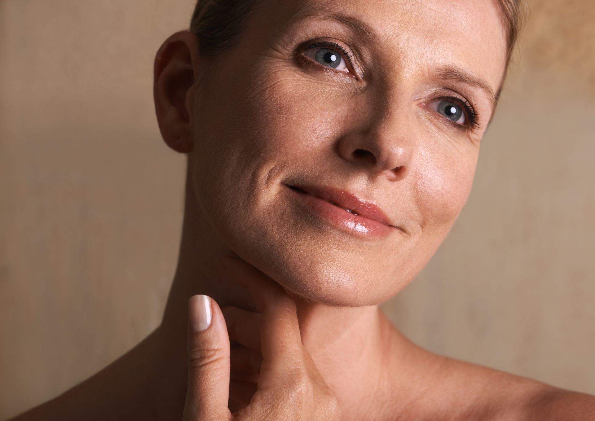 A woman is touching her neck with her hand and smiling.