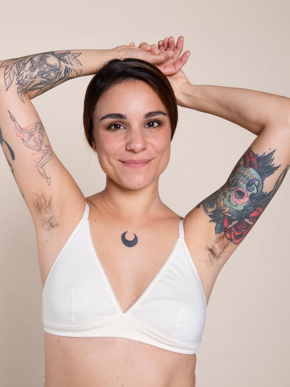A woman with tattoos on her arms is wearing a white bra
