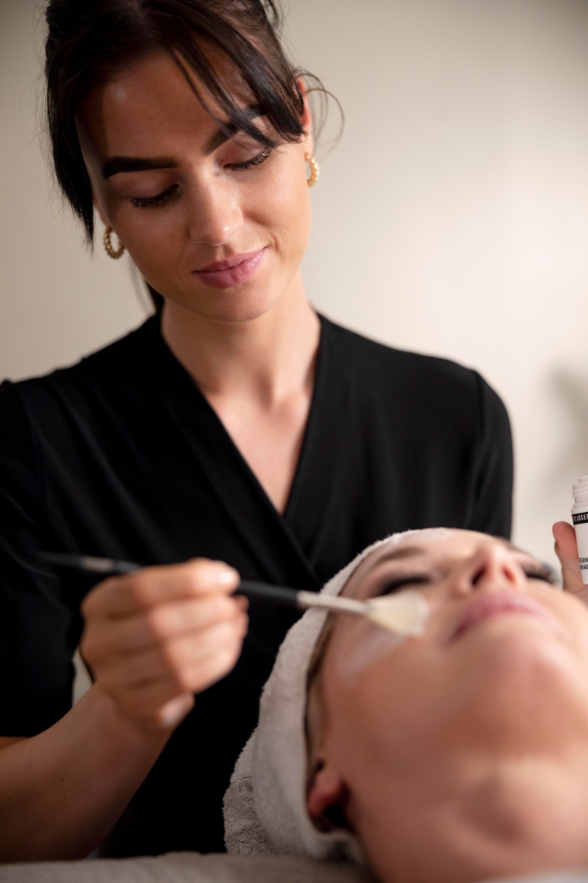 A woman is applying a facial mask to a woman 's face.