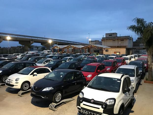 Mano di una persona che tiene il portachiavi di un'auto, mentre apre la portiera bianca di un'auto, all'aperto alla luce del giorno.