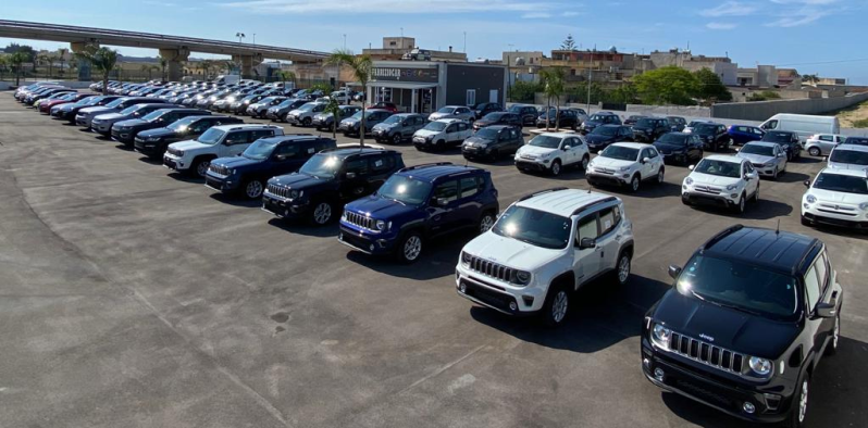 Mano di una persona che tiene il portachiavi di un'auto, mentre apre la portiera bianca di un'auto, all'aperto alla luce del giorno.