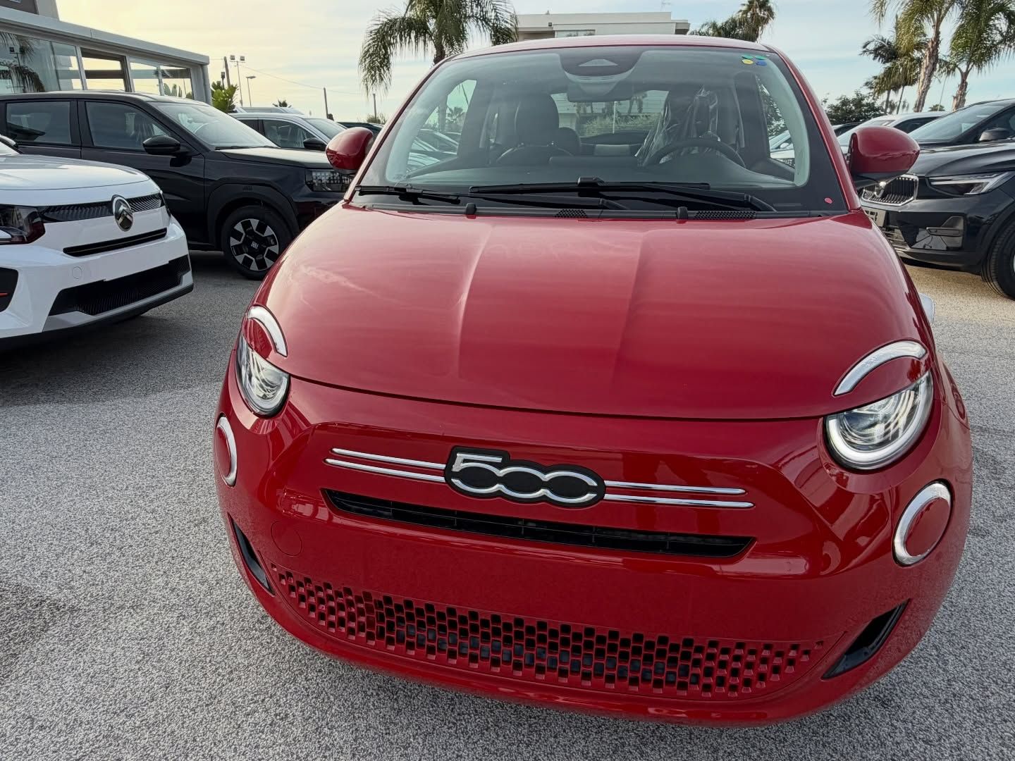Un'auto elettrica Fiat 500e rossa, con i fari rotondi, parcheggiata all'esterno, davanti a una concessionaria.