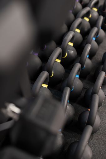 Black kettlebells with colored handles arranged in rows on a rack in a gym.