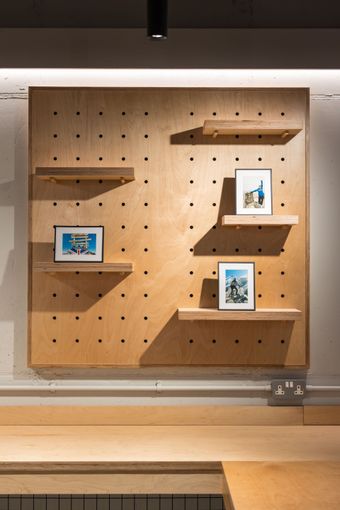 Wooden pegboard display with framed art on shelves. Tan and dark neutral color scheme.