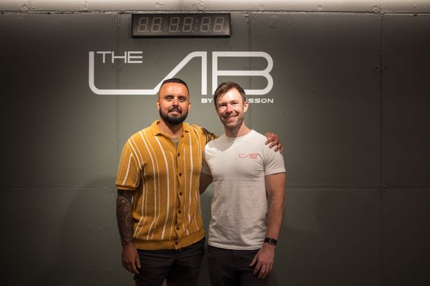 Two men posing in front of a wall with 