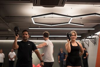 People lifting kettlebells in a gym, being instructed. Bright interior with modern lighting.
