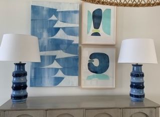 Two lamps are sitting on a table in front of three paintings
