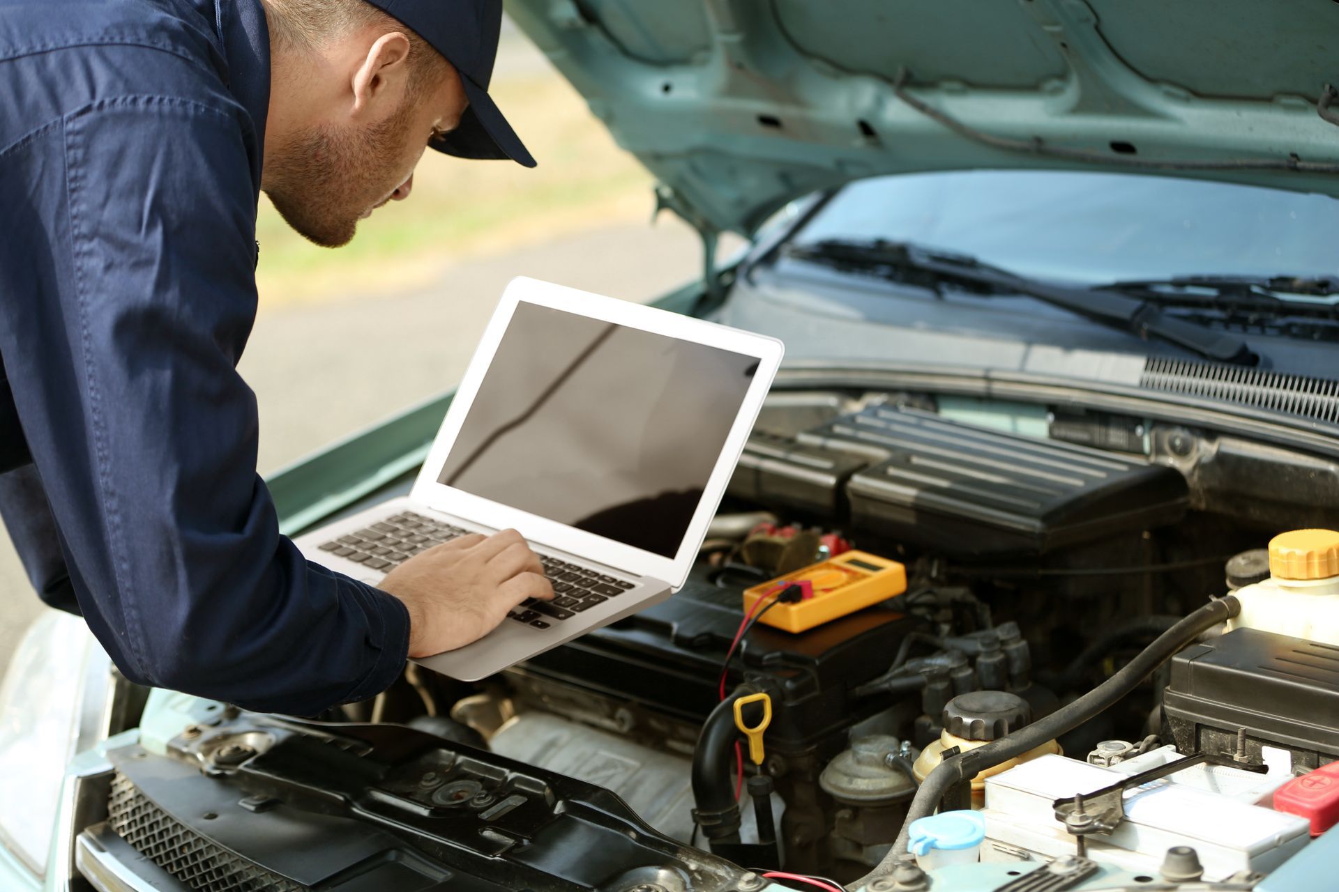 Mechanic using a laptop to diagnose a car engine under the open hood