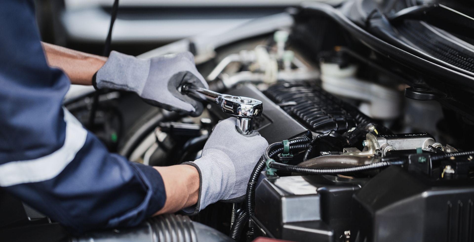 Mechanic wearing gray gloves inspecting engine components in a car hood area