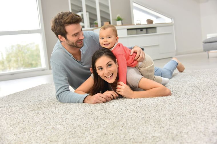 A family of three lying together on a light-colored rug in a bright, modern living room.