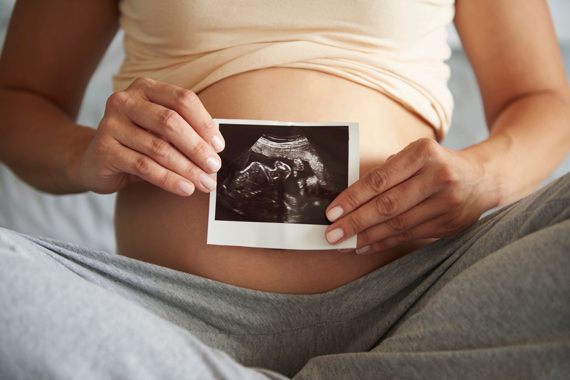 Pregnant person holding an ultrasound photo over their belly.