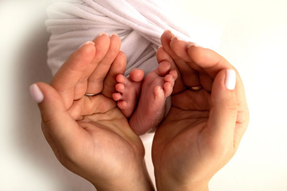 Hands cradling tiny newborn feet wrapped in white fabric.