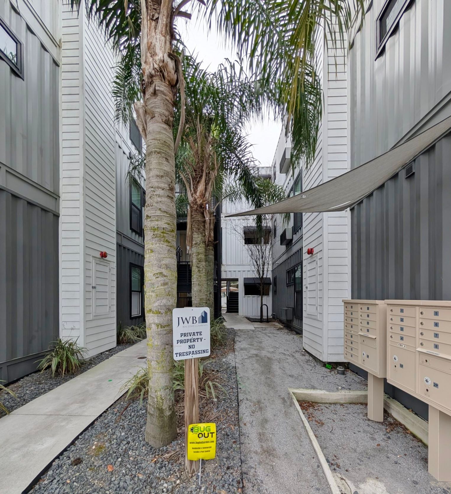 Narrow alleyway between gray buildings; palm trees and mailboxes.