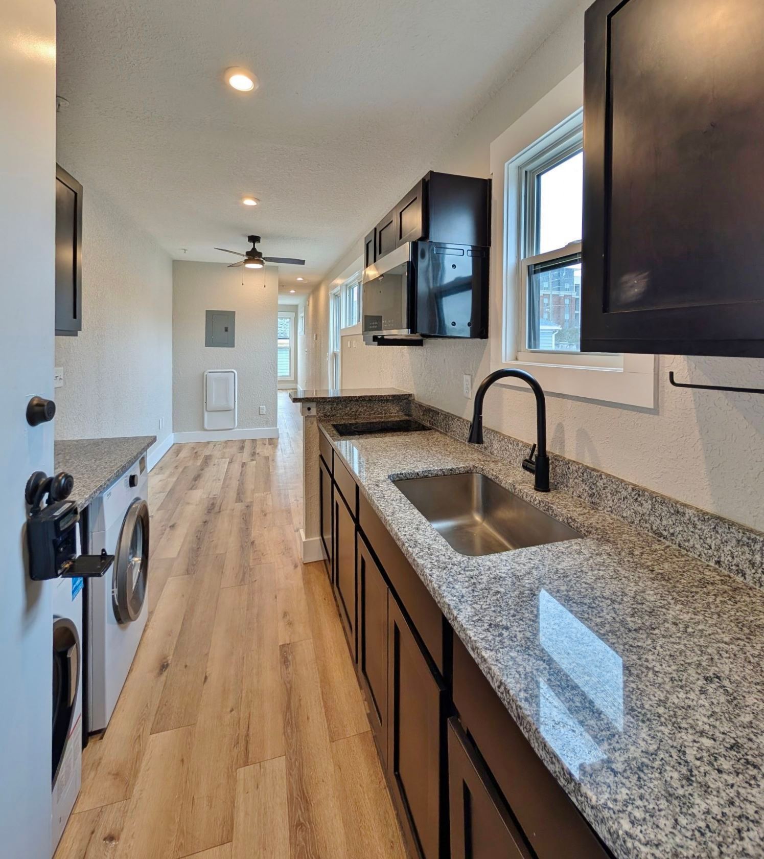 Kitchen with granite countertops, dark cabinets, stainless steel sink, and a washing machine.