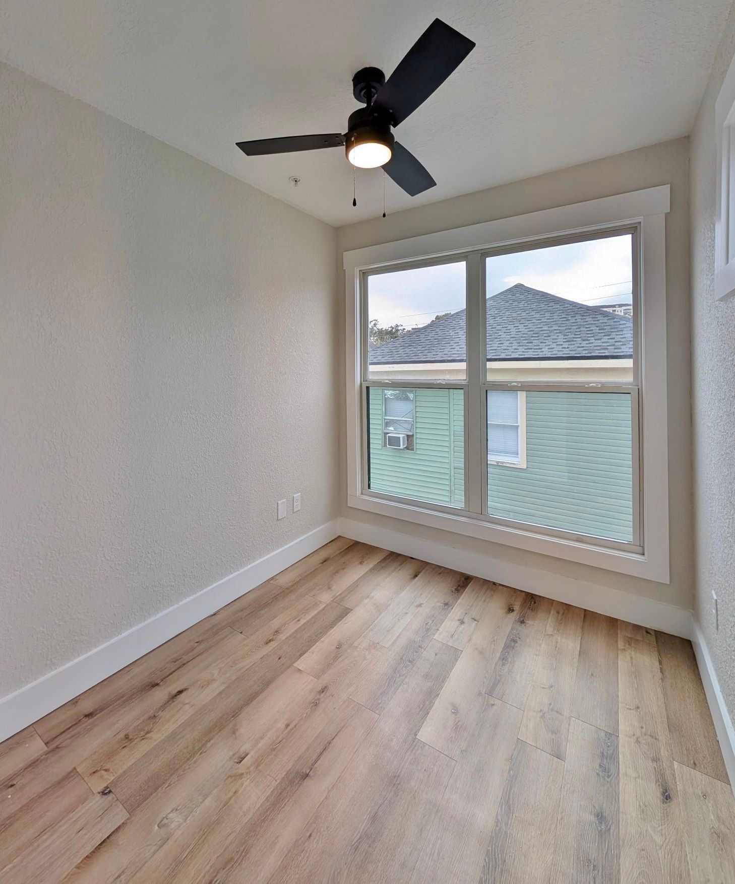 Empty room with wood floors, a window, and a black ceiling fan.