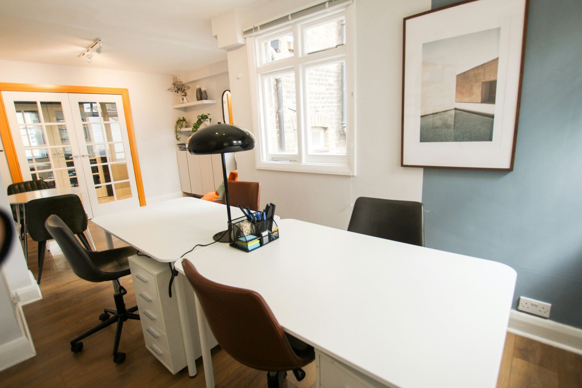 Office workspace with white desk, black chairs, artwork, and French doors.