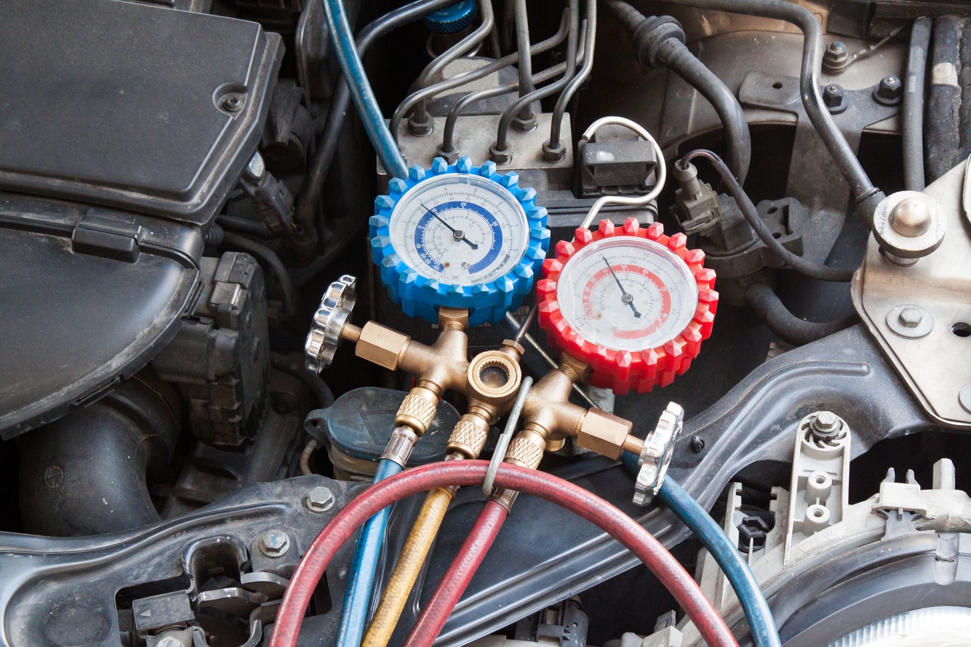 Automotive air conditioning gauge set connected to car engine, showing pressure readings with blue and red gauges.