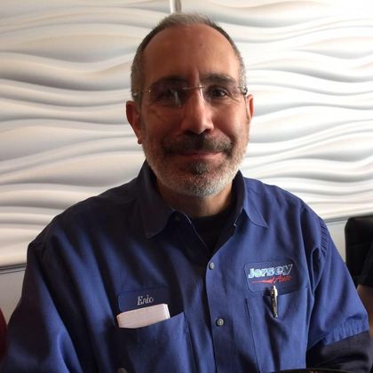 Man with glasses, graying hair, and beard in blue work shirt, smiling.