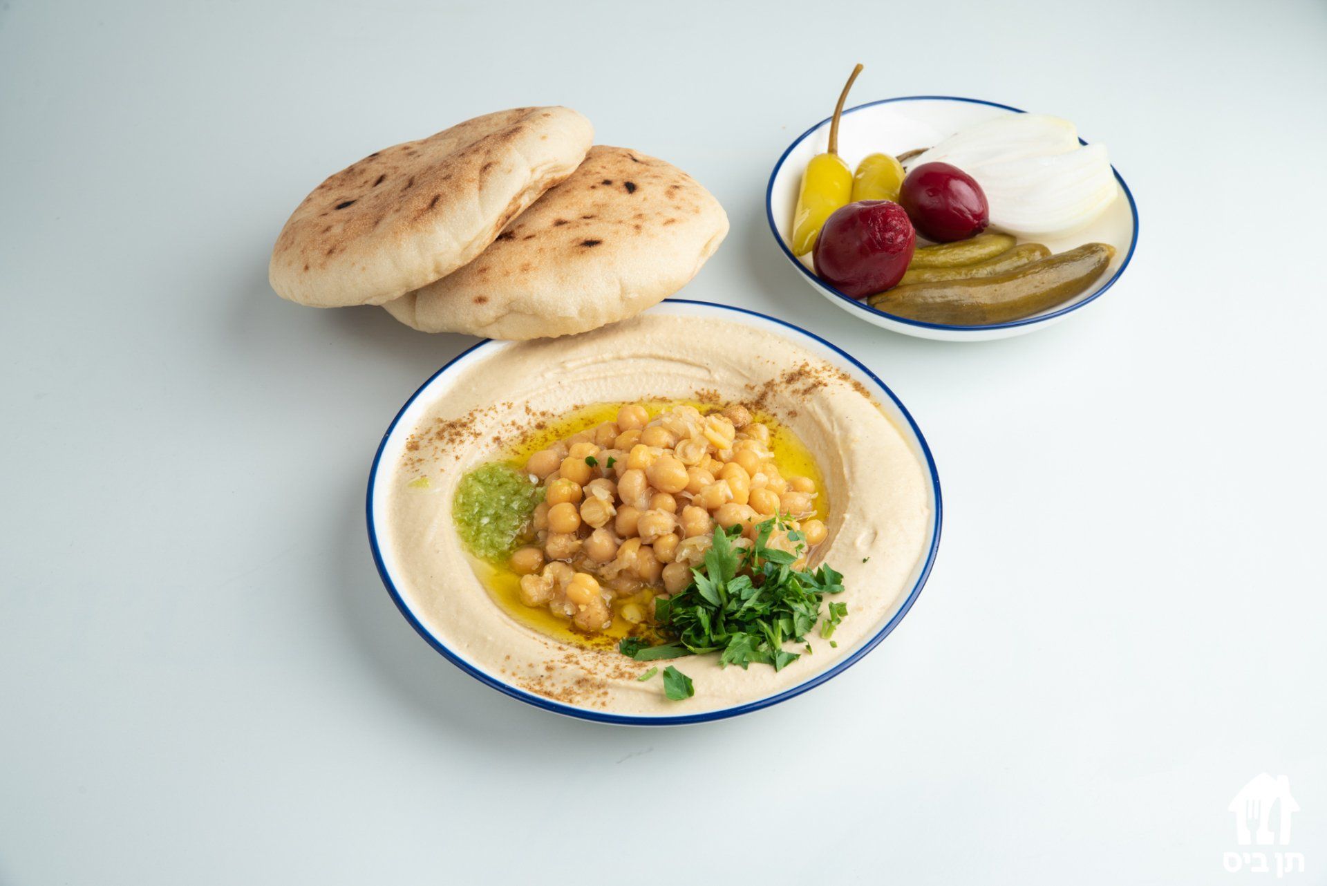 צלחת חומוס עם פיתות וחמוצים על שולחן.