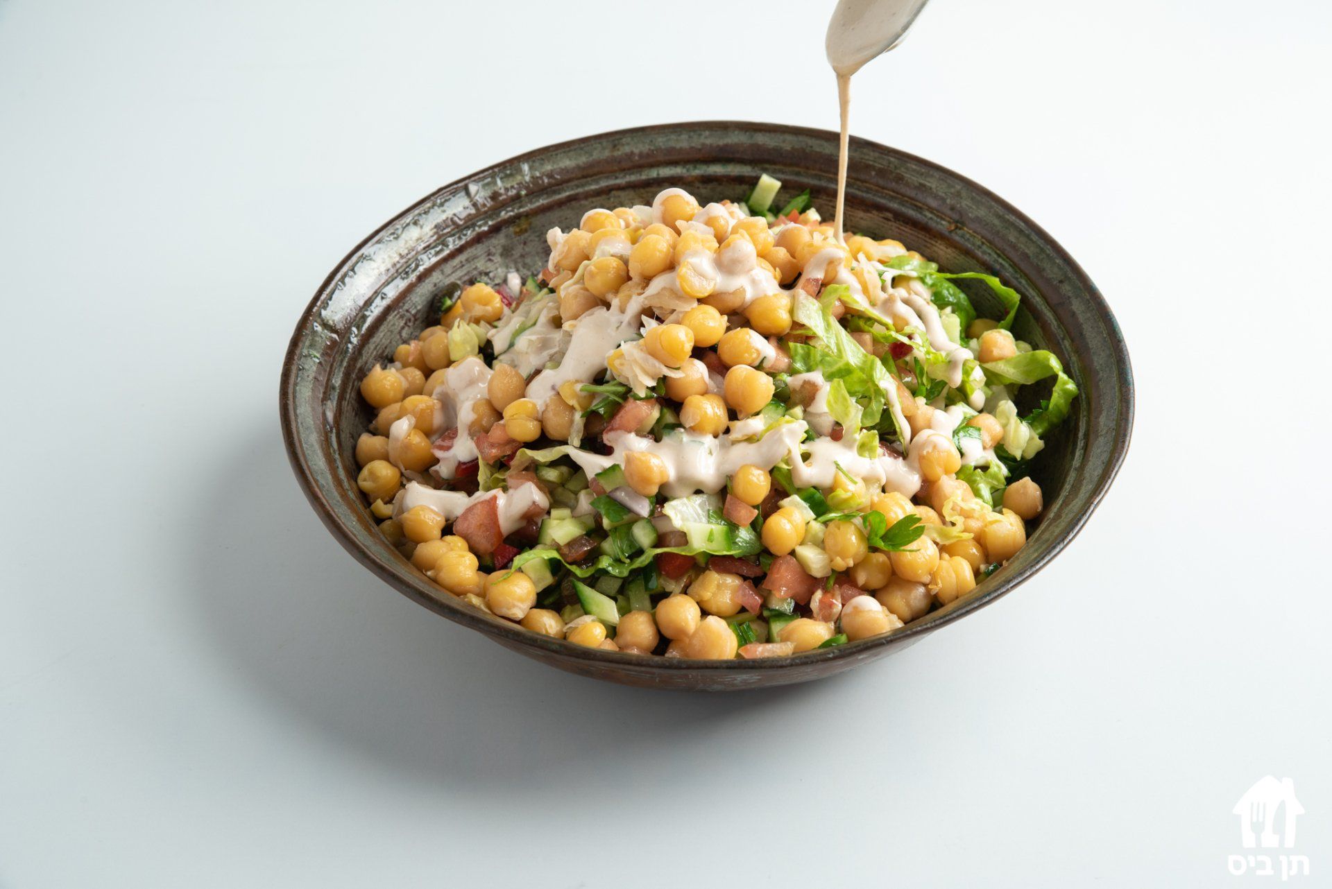 קערת חומוס וחסה ועליה יוצקים רוטב.