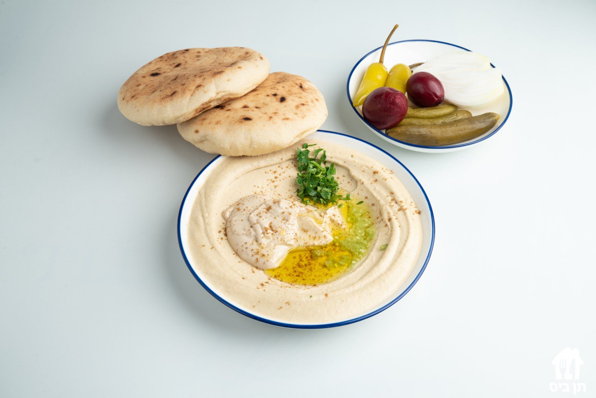 צלחת חומוס עם פיתות וחמוצים על שולחן.