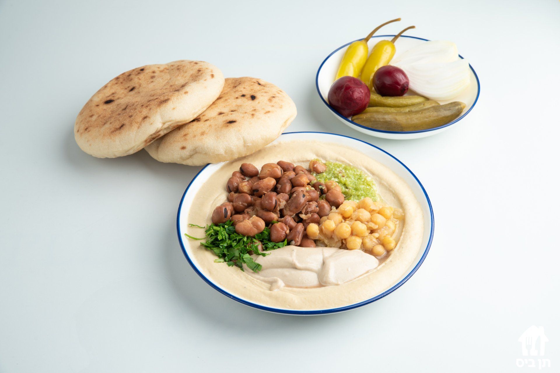 צלחת אוכל עם חומוס, חומוס, פיתות וחמוצים על שולחן.