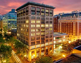 Illuminated city buildings at dusk, with a glass skybridge and warm streetlights.