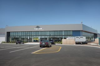 Modern storefront with glass windows, parked cars, and a white van in a sunny lot