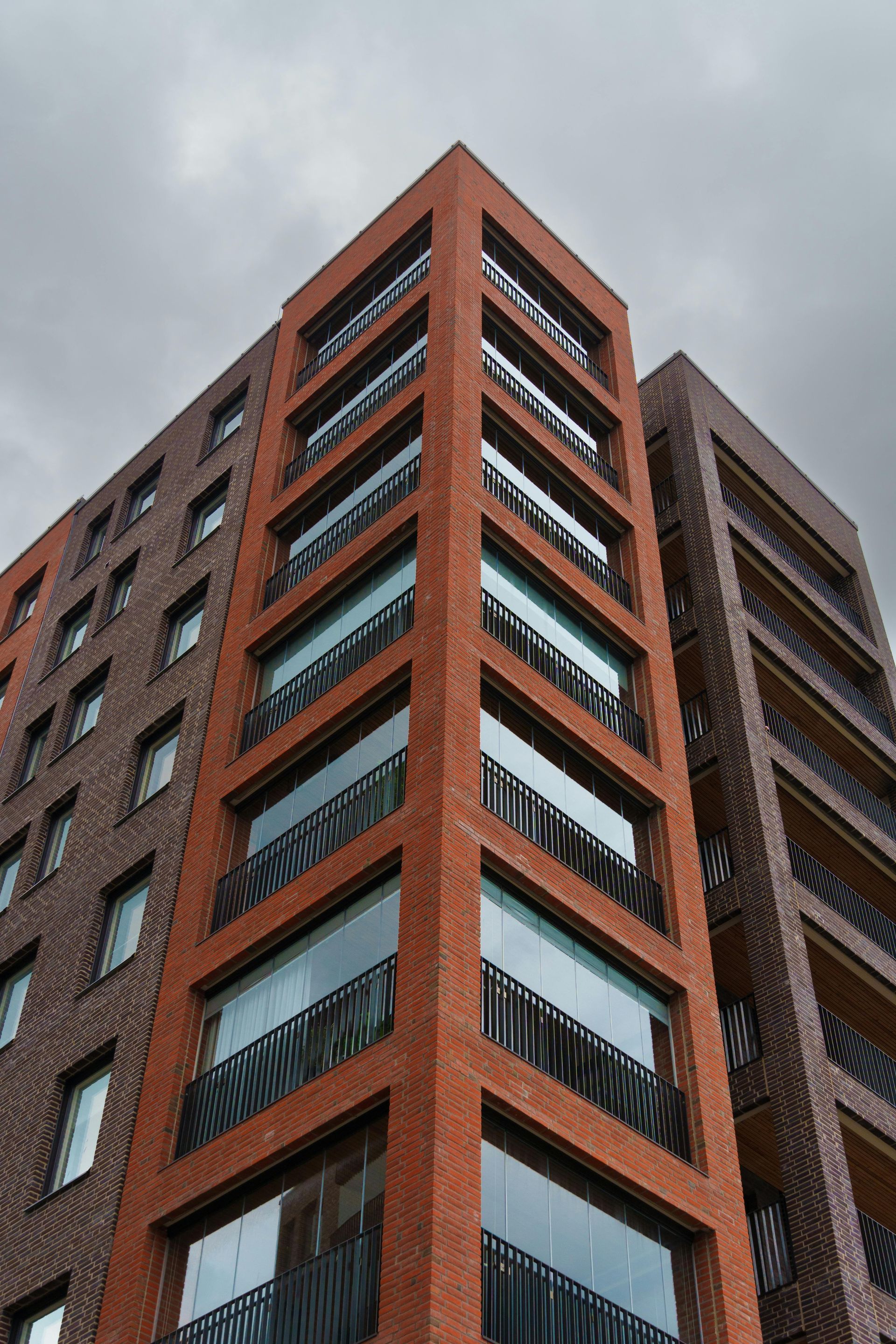 Red brick high-rise building with dark windows seen from below against a cloudy sky