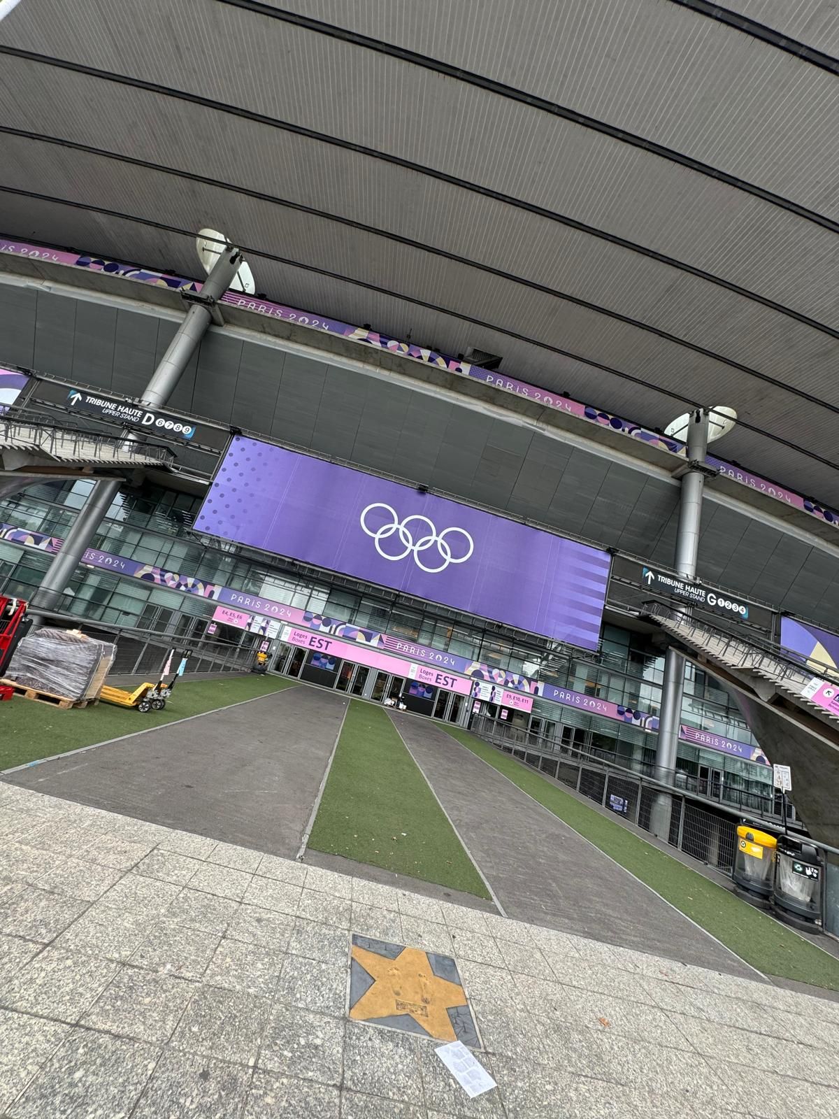 Exterior view of an Olympic stadium with the Olympic rings logo. Grey and purple color scheme.