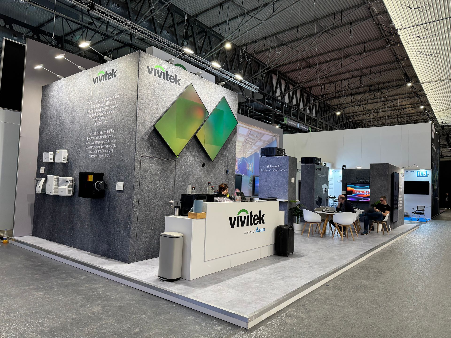 Trade show booth with gray, white, and green branding. People seated at a small table.