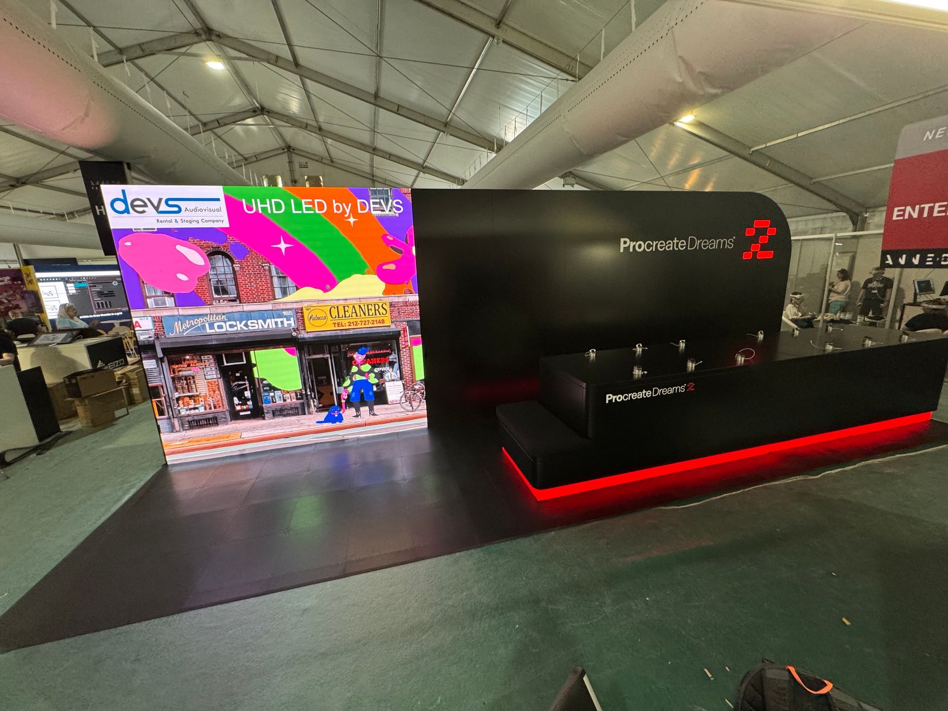 Trade show booth with a large LED screen displaying colorful art, black and red accents, and the words 