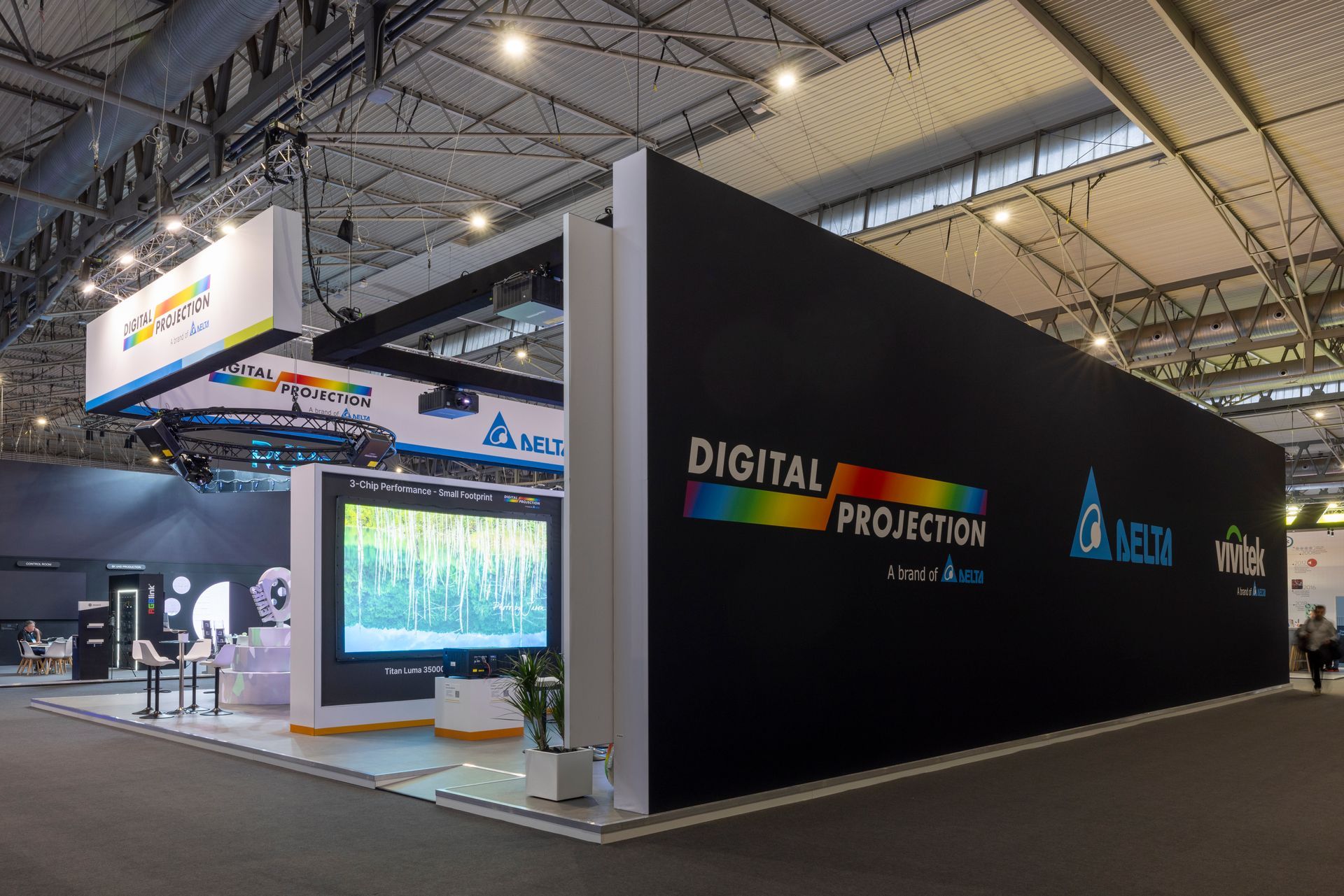 Digital Projection booth at a trade show featuring a large display screen, black walls, and brand signage.