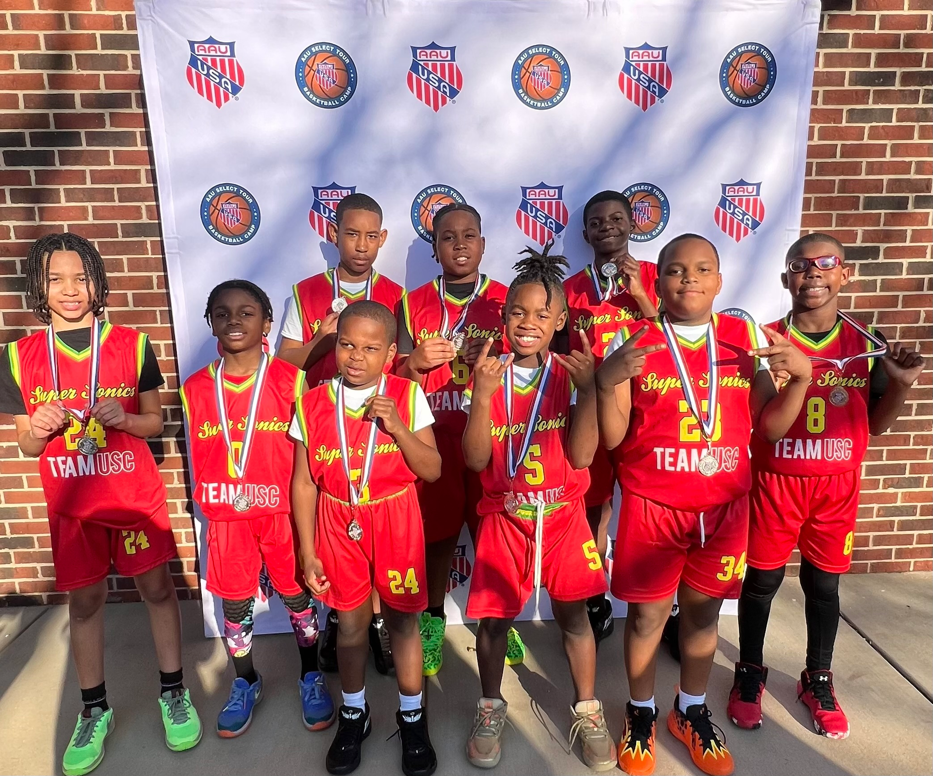 A group of young boys are standing in front of a brick wall holding medals.