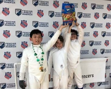 A group of young boys are posing for a picture in front of a wall that says fencing league america