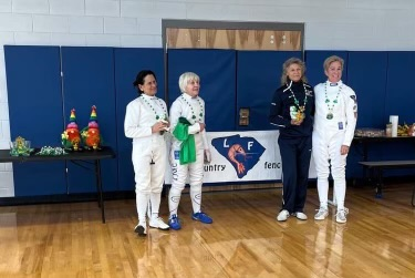 A group of women in fencing uniforms are standing in a gym
