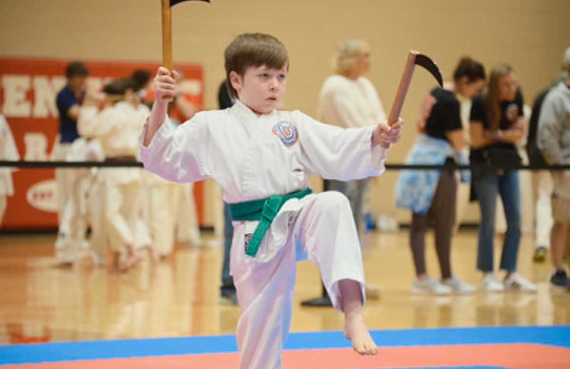 A young boy in a karate uniform is holding a wooden stick.