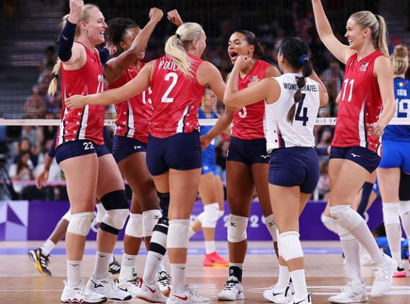 A group of female volleyball players are celebrating on a court.