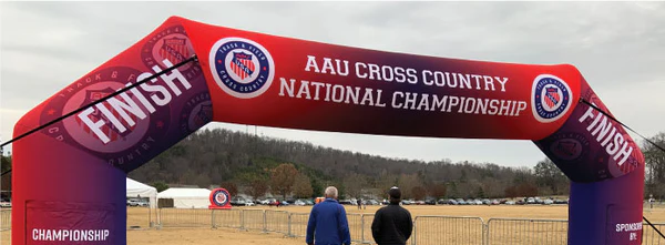 Two men are standing under a red inflatable arch for the aau cross country national championship.