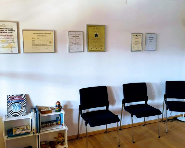 Wartebereich mit drei schwarzen Stühlen, Urkunden an der Wand.