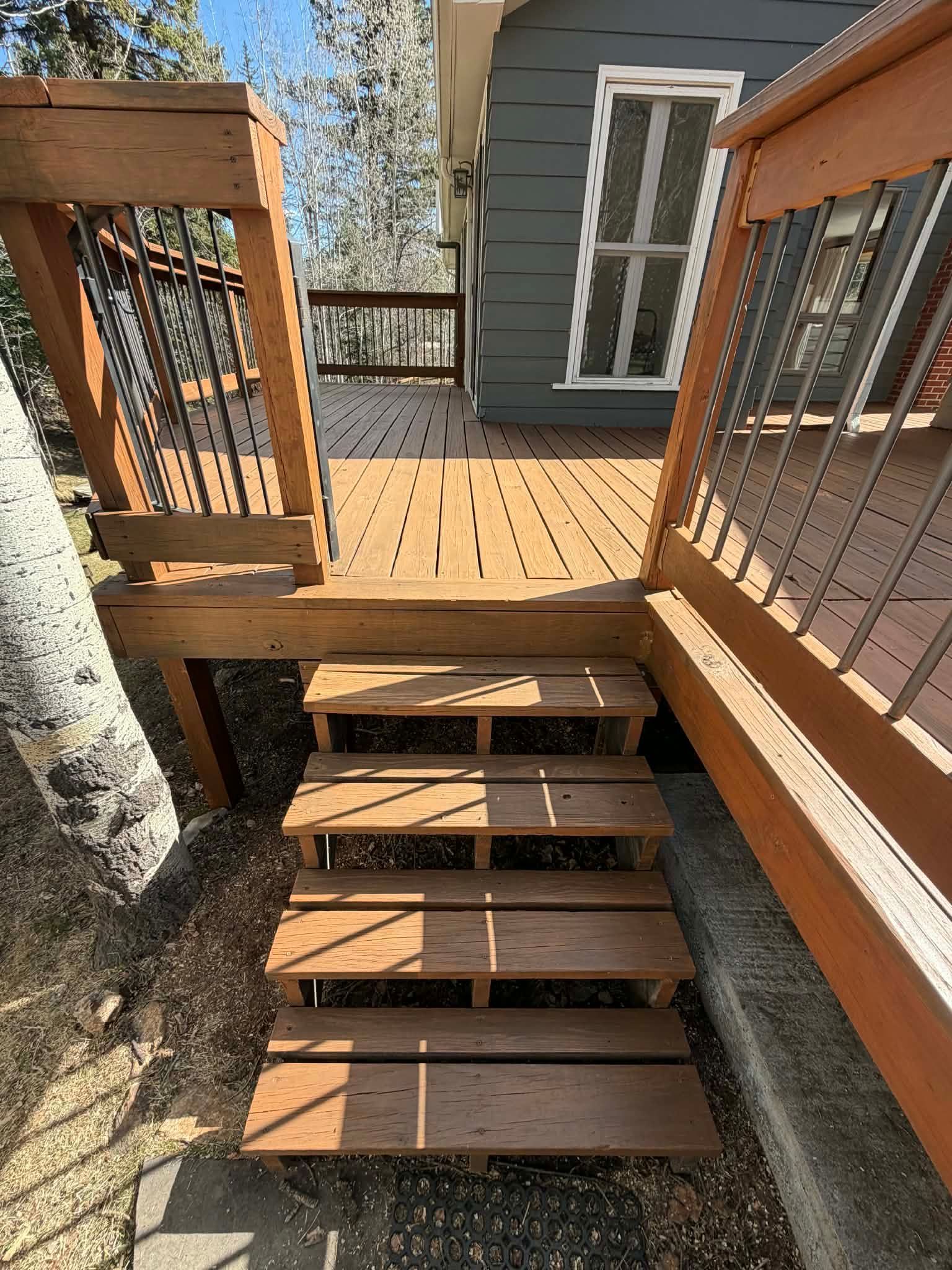 Wooden deck stairs with railings leading to a small porch beside a gray house.