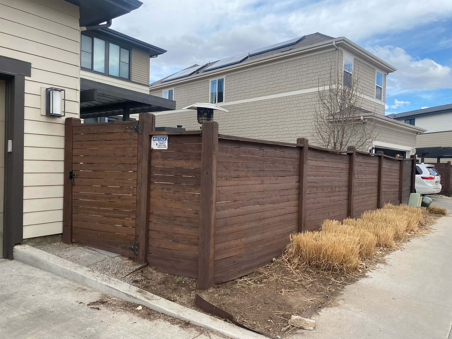 Wooden corner fence beside a modern house and driveway under a cloudy sky