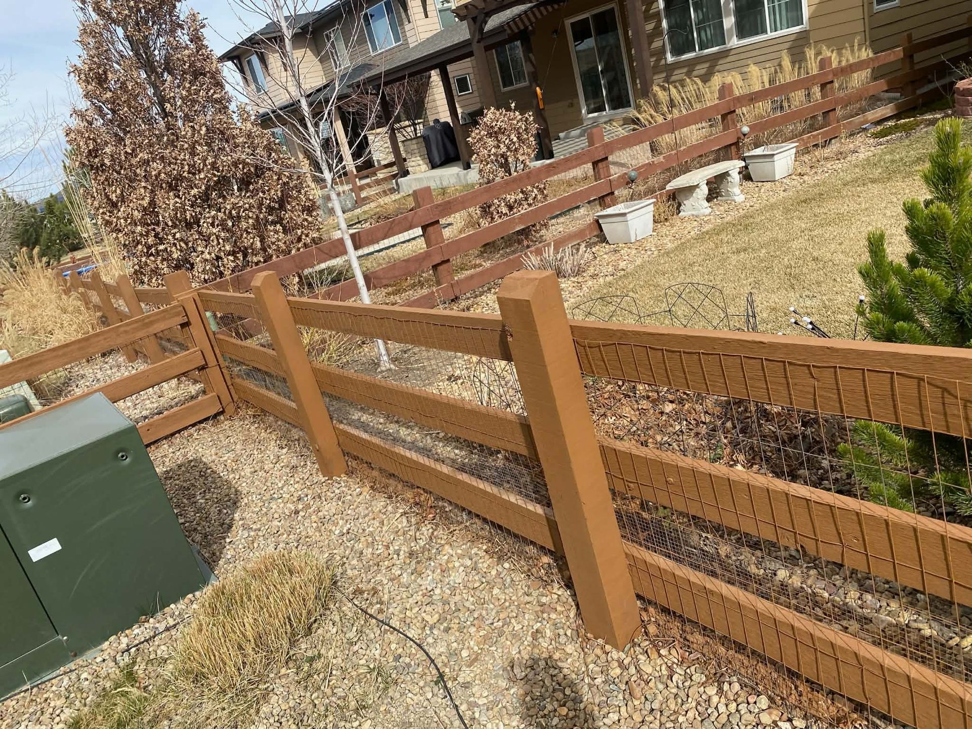 Wooden fence beside a gravel yard with a house and retaining wall in the background