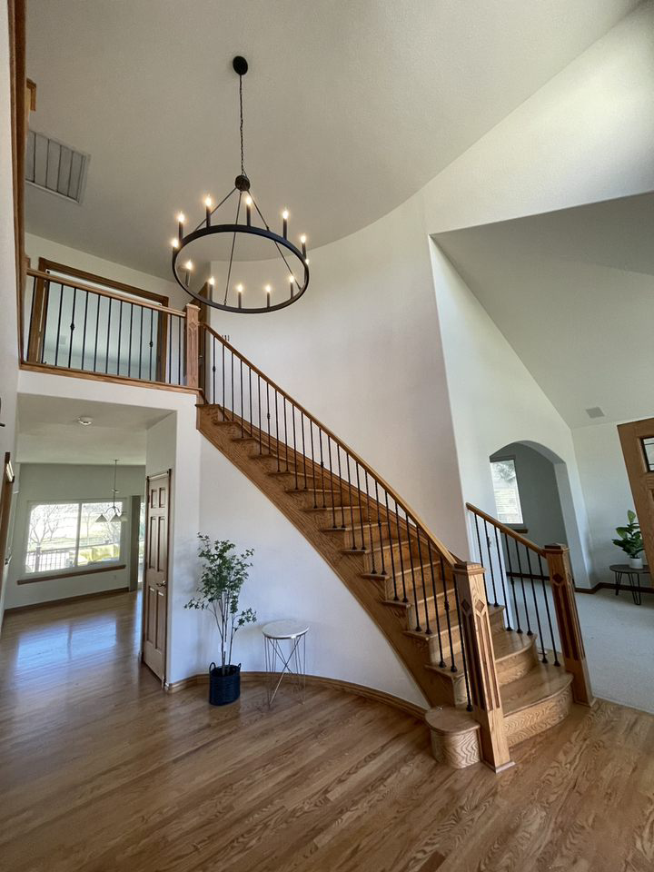Bright foyer with a wooden staircase, chandelier, and hardwood floors in a modern home.