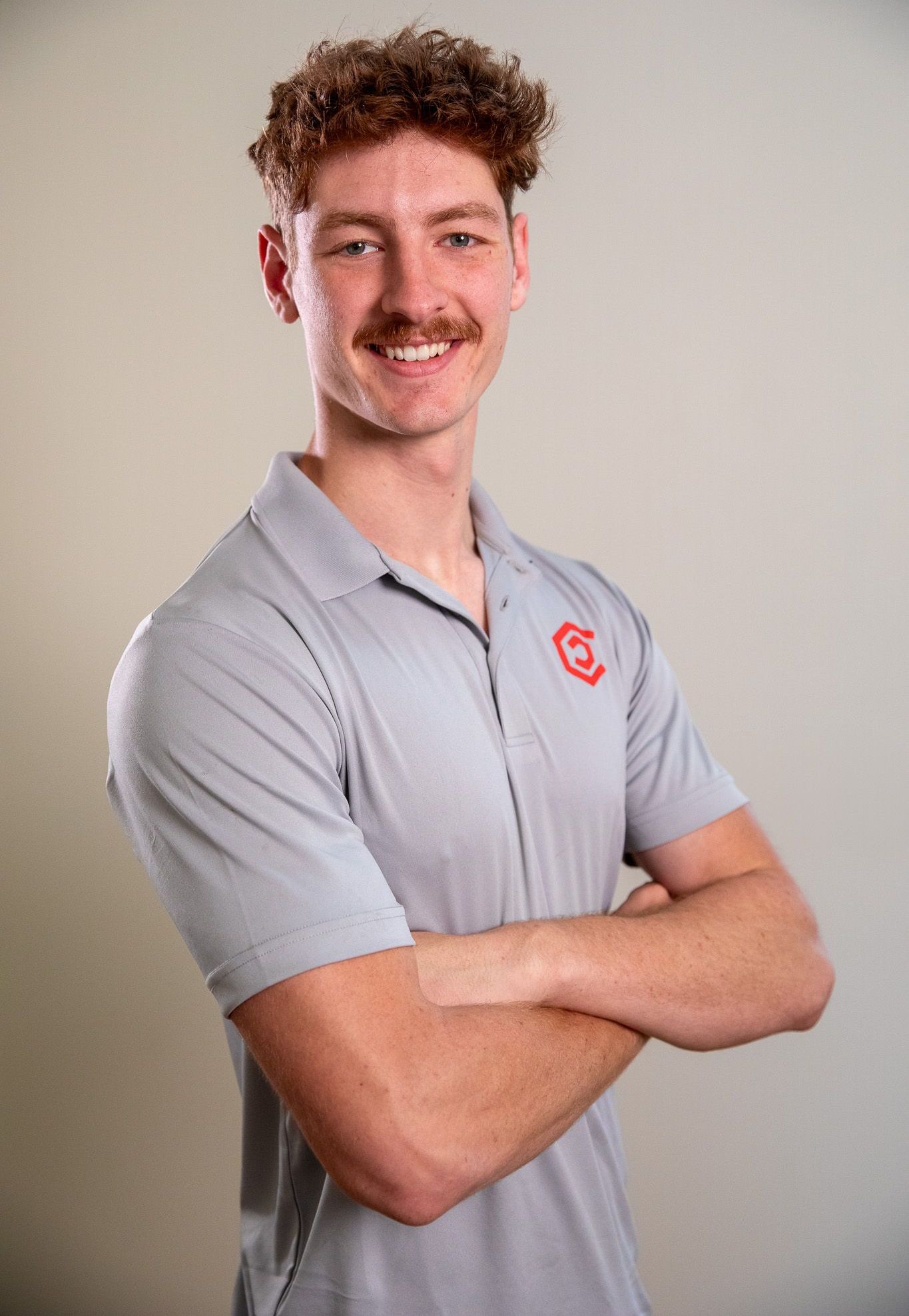 A young man is in a Center Home Improvement shirt standing with his arms crossed and smiling.